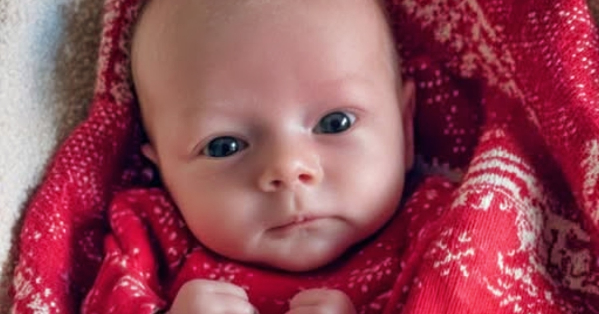 Un nouveau-né emmailloté, les yeux grands ouverts, regarde avec curiosité.