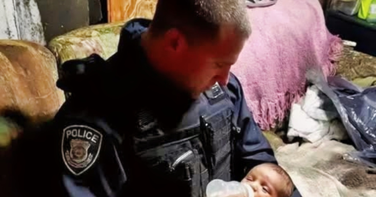Un homme en uniforme tient délicatement un bébé emmitouflé dans sa veste, dans un cadre sombre qui évoque un bâtiment abandonné.