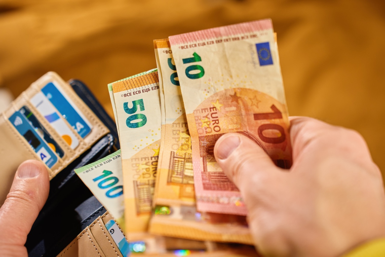 Personne tenant des billets de banque, l'air serein, avec une décoration d'intérieur en arrière-plan.