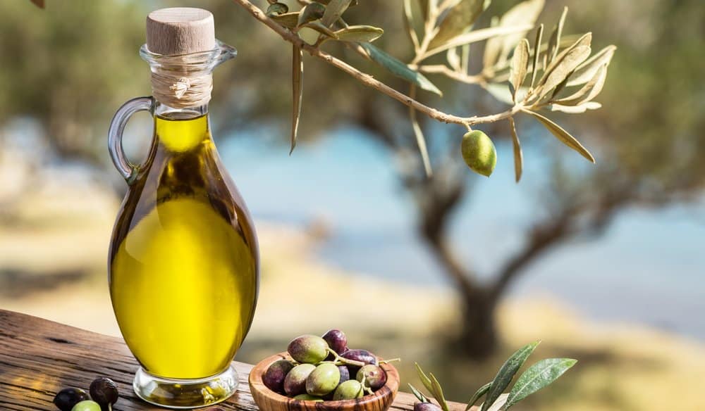 Un flacon d'huile d'olive à côté d'une coupelle de produit cosmétique