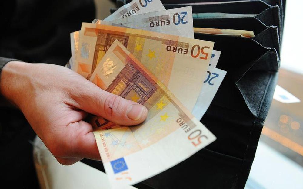 Une main tenant des billets de banque à côté d'une tirelire en forme de cochon sur une table.